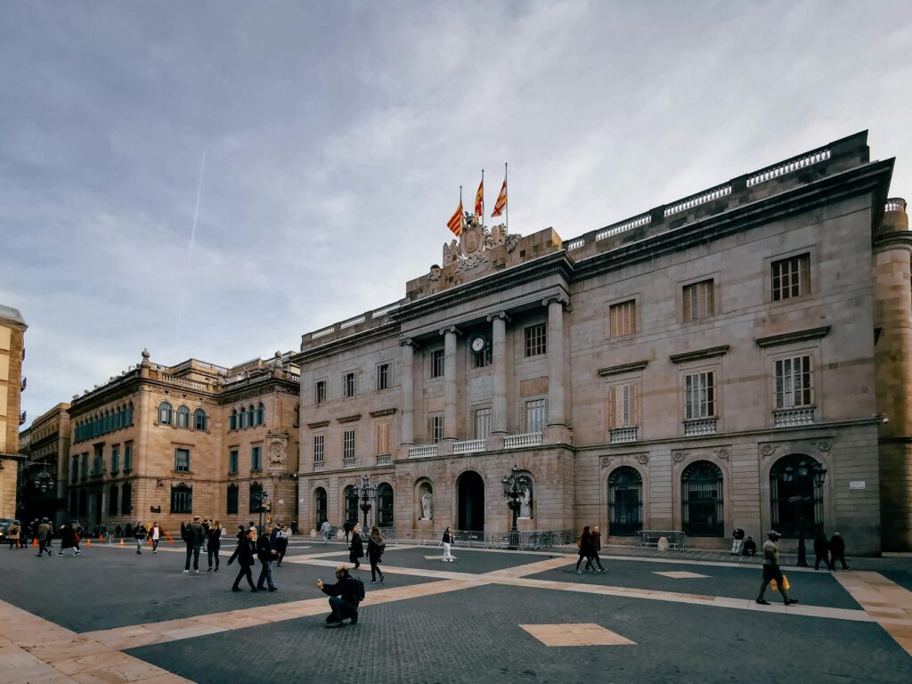 Explore a bustling public square in Spain, surrounded by historic buildings under a cloudy sky.